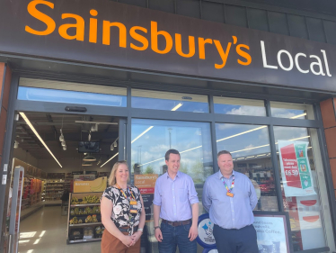 Tom posing for a photograph with two staff members outside of the entrance to Sainsbury's Local in Priors Hall.